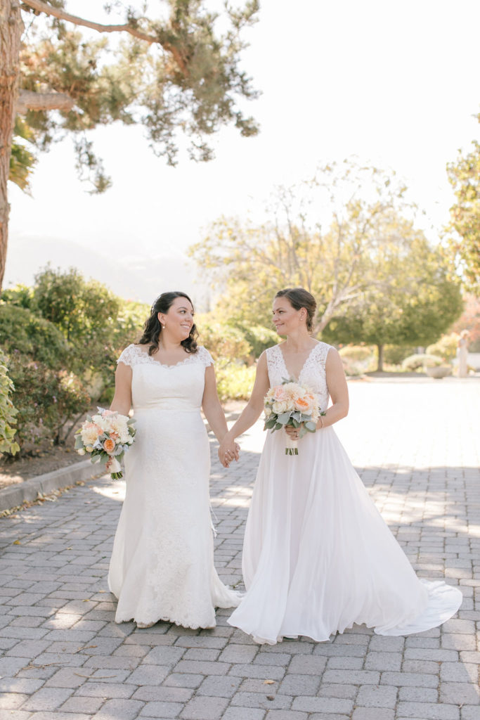 Two brides walking hand in hand down a scenic path in carmel at Folktale winery