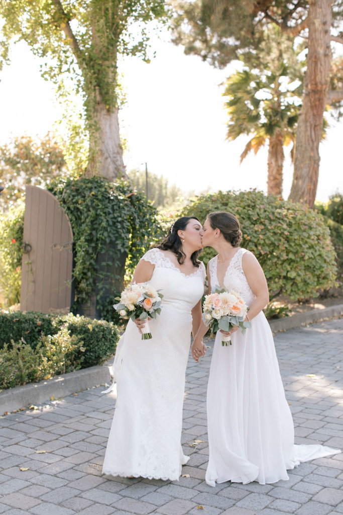 two brides kissing and holding peach and cream colored bouquets