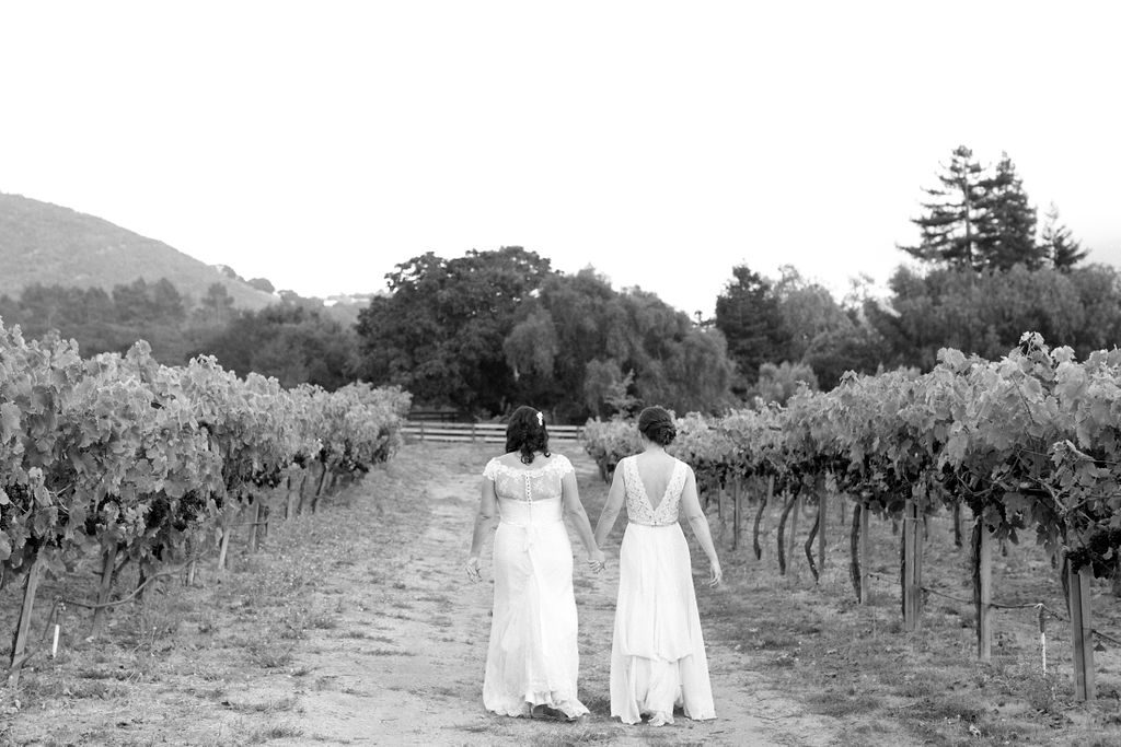 black and white image of two brides walking down path together in winery
