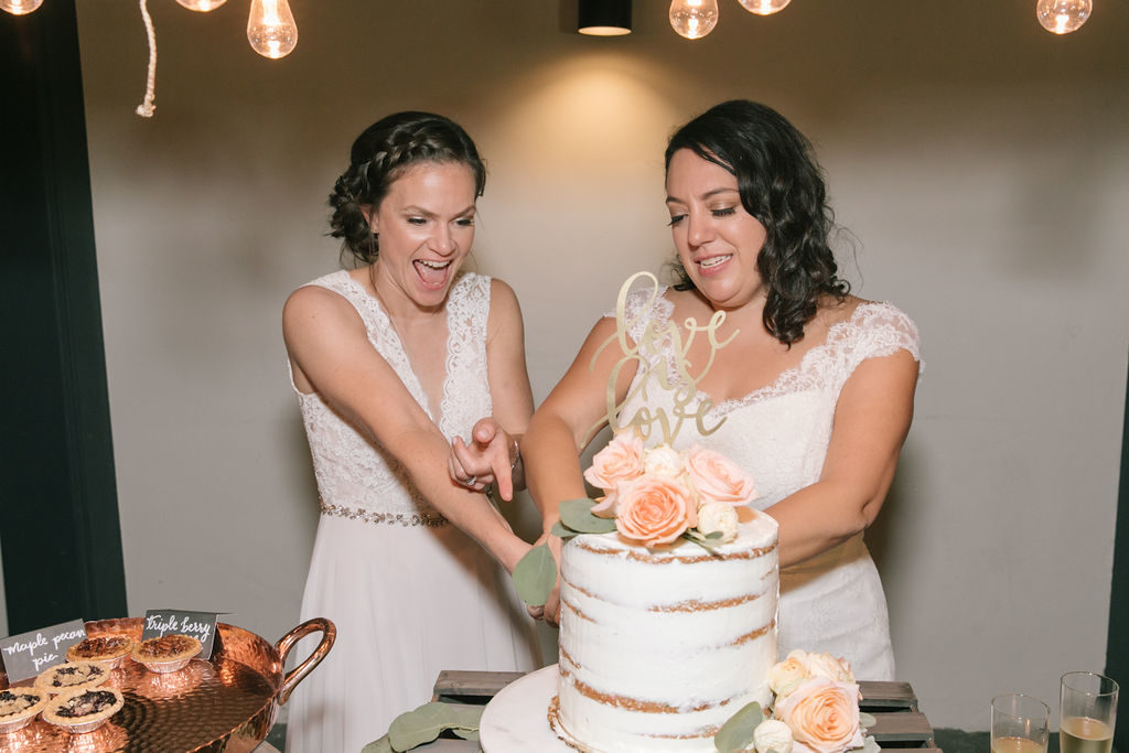two brides cutting a wedding cake at their wedding reception with a topper stating love is love