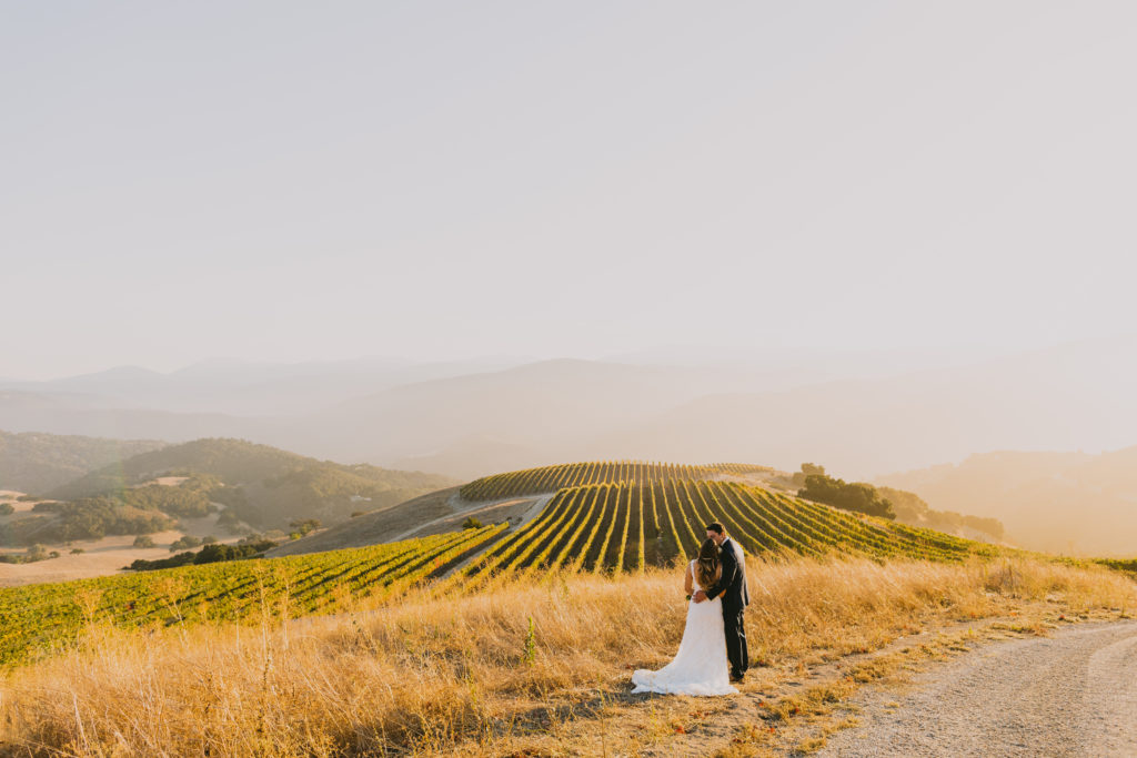 Couple hugging and looking out over vineyards at sunset at the wedding venue holman ranch in carmel