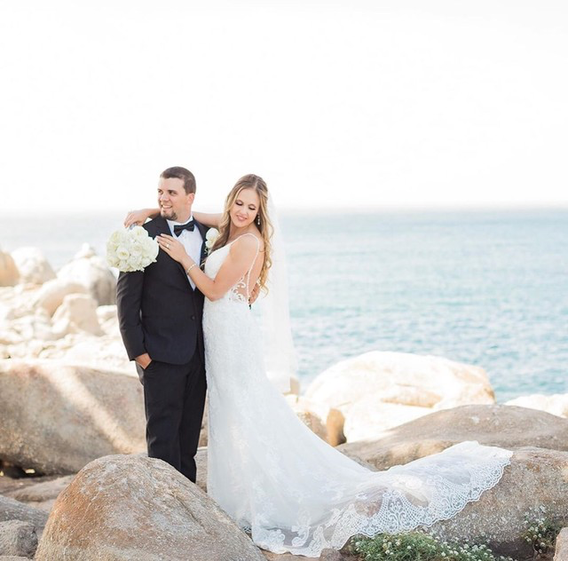 Recently married bride and groom on rocks in front of the ocean in Monterey, CA with white traditional bouquet