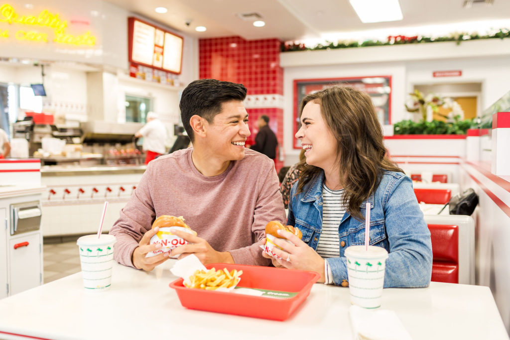 engaged couple smiling at each other and laughing while eating hamburgers at in and out in california