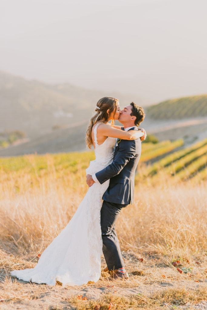 Couple kissing up above the vineyard at Holman Ranch