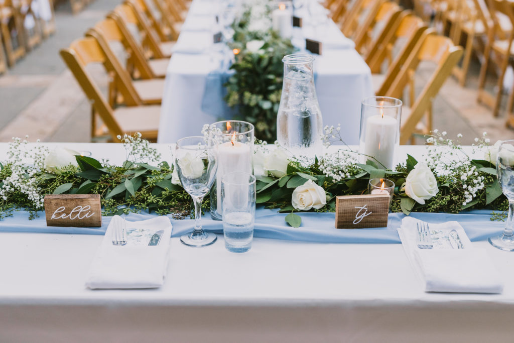 Long banquet table with ivory linen and dusty blue runner with eucalyptus garland down the center. 
