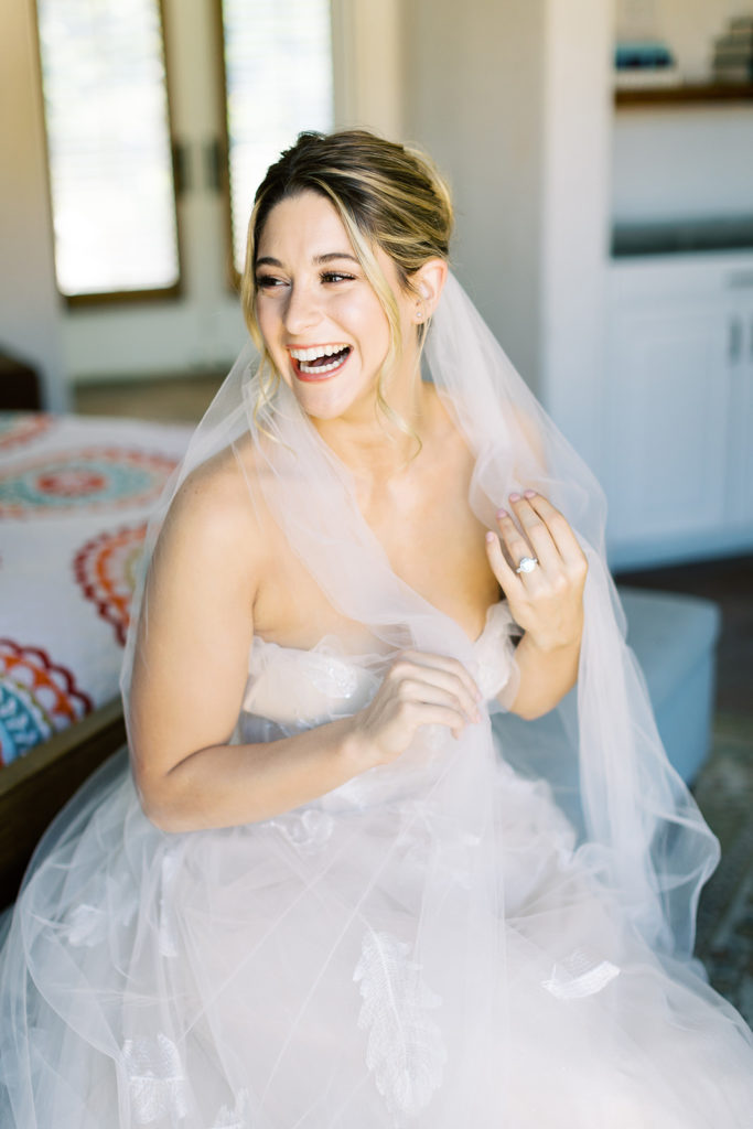 Bride smiling holding veil in a dress with feather details